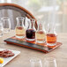 An Acopa flight tray with glass carafes filled with brown liquid on a table.