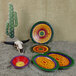 An Elite Global Solutions oval melamine platter with a colorful circular pattern on a table with cactus and colorful plates.