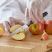 A person in a white coat using a Mercer Culinary pointed tip paring knife to slice an apple.