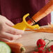 A hand holding a Mercer yellow "Y" vegetable peeler peeling a carrot.