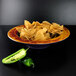 A multi-color melamine bowl of chips with jalapenos and a green pepper.