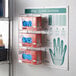 A Noble Products wire wall mount glove dispenser station with three boxes of gloves.