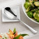 An Acopa Edgeworth stainless steel serving spoon in a bowl of brussels sprouts on a table.