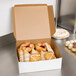 A 12" x 12" white bakery box full of pastries on a counter.