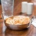 An American Metalcraft stainless steel balti dish filled with pasta and sauce on a table with a glass of water.