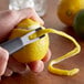 A person using a Mercer Culinary channel knife to peel a lemon over a counter.