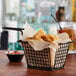 A black wire rectangular fry basket filled with fried food on a table.