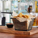 A black rectangular mini fry basket filled with fried food on a wooden table.