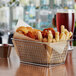 A rectangular chrome fry basket filled with fries on a table.