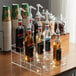 A clear acrylic Choice 3 Tier syrup bottle holder on a counter with bottles of liquid.