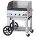 A Crown Verity stainless steel mobile grill with a lid on a cart with wheels.