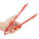 A hand holding a pair of red Carlisle plastic utility tongs.