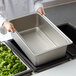 A person holding a Vollrath stainless steel spillage pan with a tray of broccoli.