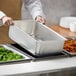 A person using a Vollrath aluminum steam table spillage pan to serve broccoli at a salad bar.