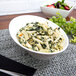 A white porcelain pinch bowl filled with pasta, spinach, and cheese.