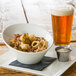 A Whittier white porcelain pinch bowl filled with food on a table next to a glass of beer.