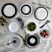 A table set with white and black Arcoroc plates and bowls with a white Arcoroc serving bowl filled with green leaves.