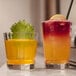 Two Chef & Sommelier highball glasses with yellow drinks and garnishes on a counter.