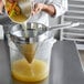 A person using a Choice Fine China Cap Strainer to pour yellow liquid into a pot.
