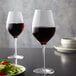 Two Stolzle Bordeaux wine glasses filled with red wine on a table with salad.