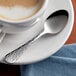 An Acopa stainless steel demitasse spoon on a saucer with a cup of coffee.