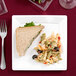 A sandwich and pasta salad on a white square plastic plate.