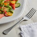 An Acopa Vernon stainless steel salad fork on a plate of salad with cucumbers and watermelon.