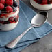 An Acopa stainless steel oval bowl dessert spoon next to a glass of yogurt with berries.