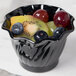 A black Cambro plastic swirl bowl filled with fruit on a counter.