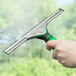 A hand with a green and black Unger ErgoTec squeegee handle cleaning a window.