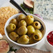 A white plate with green olives, cheese, and crackers.