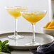 Two Arcoroc coupe cocktail glasses with orange drinks and a garnish of mint on a plate.