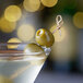 A Belosa green olive with a hole in it on a wooden stick in a martini.