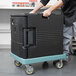 A man pushing a slate blue Cambro Camdolly with a black container inside.