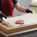 A person in a red apron cutting meat on a white cutting board.