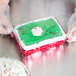 A person in gloves holding a rectangular holiday cake in a Durable Packaging foil bake pan with a clear dome lid.