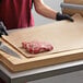 A person cutting meat on a Choice natural kraft freezer paper-covered cutting board.