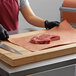 A person cutting a piece of meat on a table using 12'' PeachTREAT® Butcher Paper.