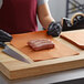 A person in black gloves using a large knife to cut peach steak paper on a cutting board.