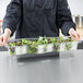 A chef holding a Carlisle clear plastic food pan filled with green leaves.