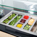 A Carlisle clear polycarbonate food pan filled with vegetables and greens on a counter.