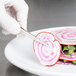 A hand in a glove uses a Mercer Culinary plating knife to cut a radish on a plate.