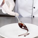 A chef using a spoon to pour chocolate syrup on a plate.
