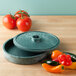 A green HS Inc. polyethylene tortilla server with a lid and tomatoes and peppers next to it.