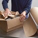 A person using Lavex natural kraft void fill packing paper to open a box.