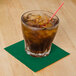 A Hunter green Hoffmaster beverage napkin under a glass with a straw and brown liquid.