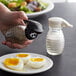 A hand holding a Tablecraft beehive glass pepper shaker with a black top over hard boiled eggs.
