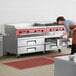 A woman in a professional kitchen opening a drawer in an Avantco 84" 4 drawer refrigerated chef base.