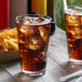 A Libbey Tritan plastic stackable mixing glass filled with cola and ice on a table with fries.