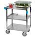 A Carlisle stainless steel utility cart with a plastic container of vegetables on it.